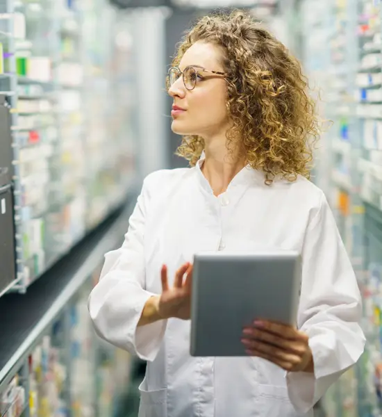 Female pharmacist with digital tablet managing medications in pharmacy storage.