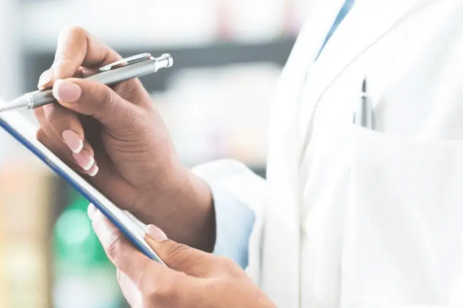 Doctor in white coat writing notes on clipboard with pen