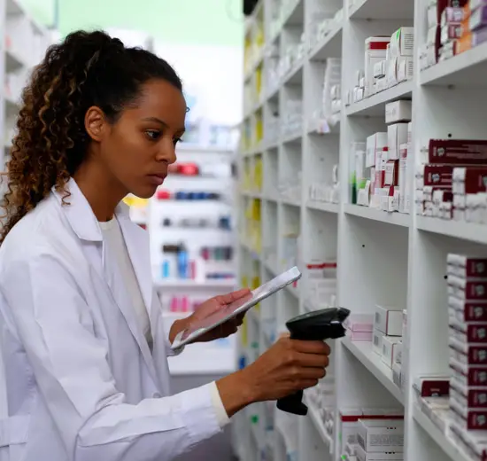 Female pharmacist scanning medication boxes and managing inventory in pharmacy storage.