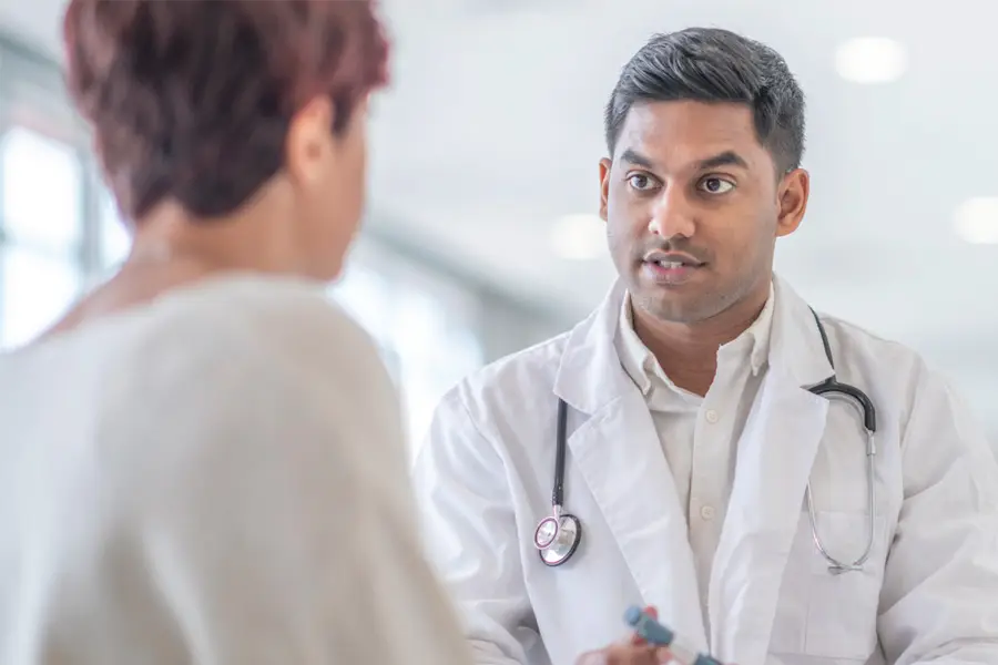 Doctor with stethoscope talking to patient during medical consultation in a hospital.