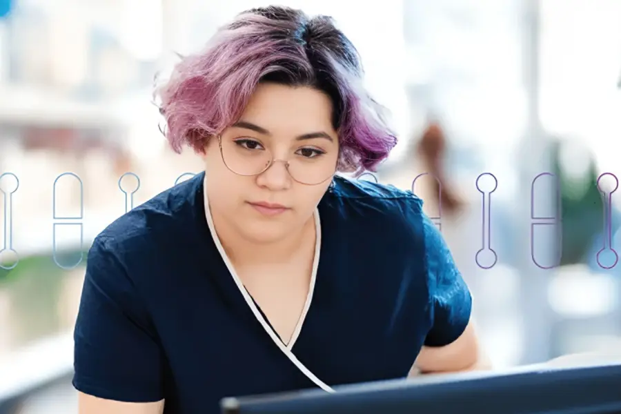 Healthcare worker in navy scrubs with glasses reviewing information on computer