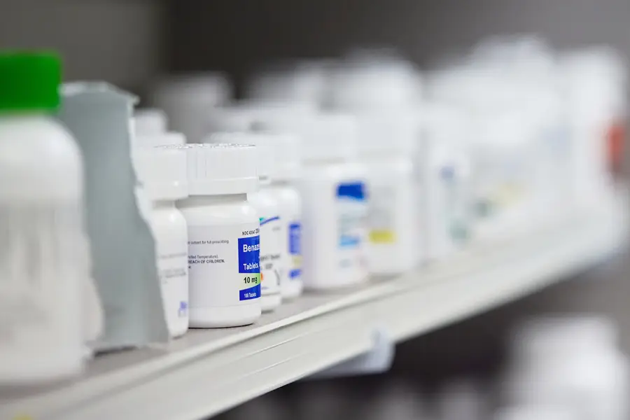 Close-up of prescription pill bottles lined up on pharmacy shelf