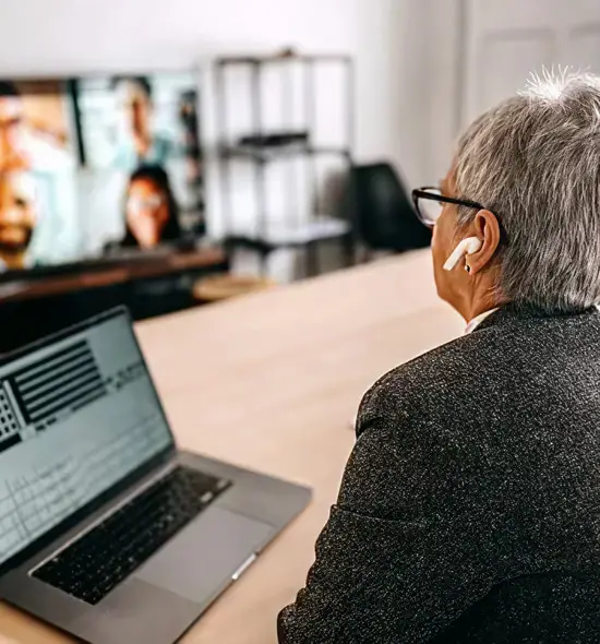 Senior professional using a laptop and earbuds for a virtual telehealth or business video conference.