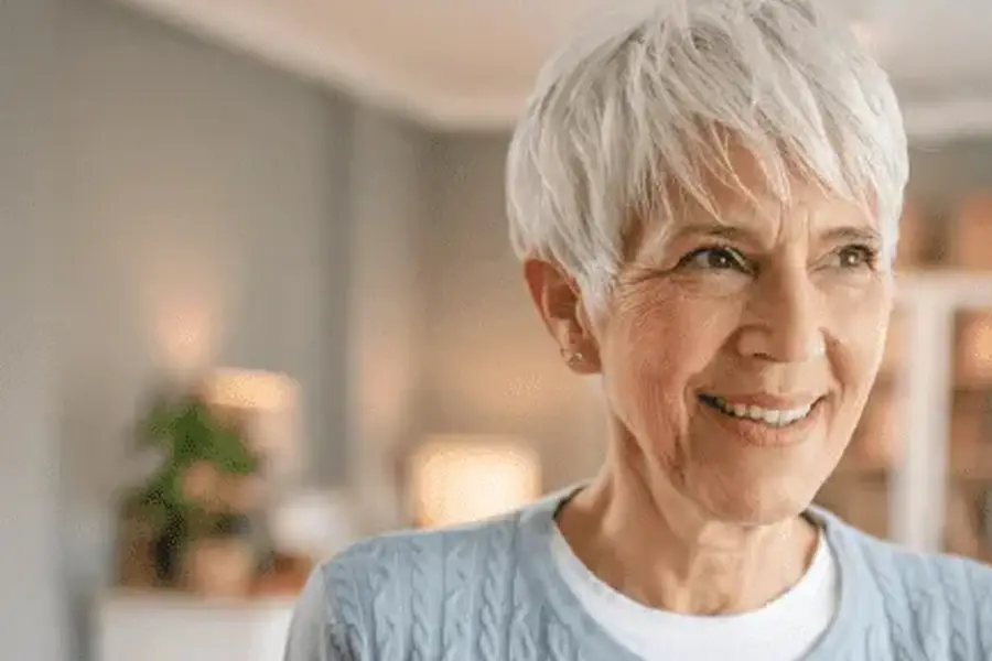 Smiling senior woman with short white hair looking away while standing at homemiling senior woman with short white hair looking away while standing at home