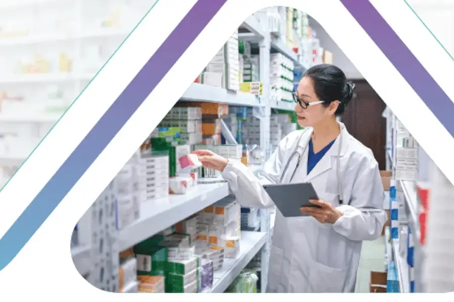 Pharmacist in white coat using tablet while checking medicine inventory on pharmacy shelves"