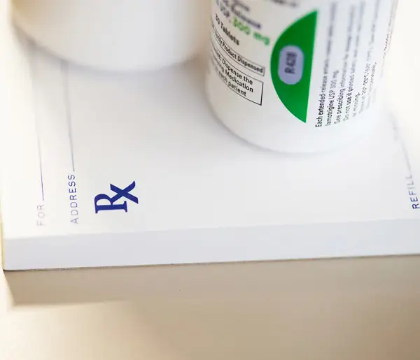 Prescription pad with Rx symbol and pill bottle, representing medication refills and pharmacy services.