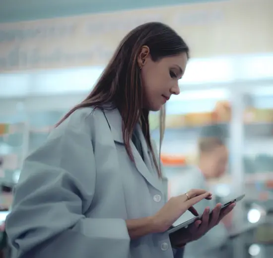 Female pharmacist in white coat using a digital tablet to manage prescriptions in a pharmacy