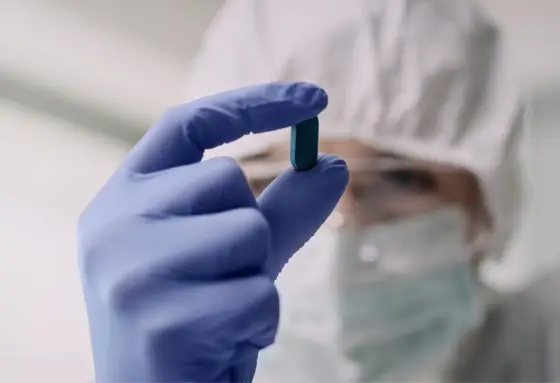 Scientist in protective gear holding a blue pill with gloved hand in laboratory"