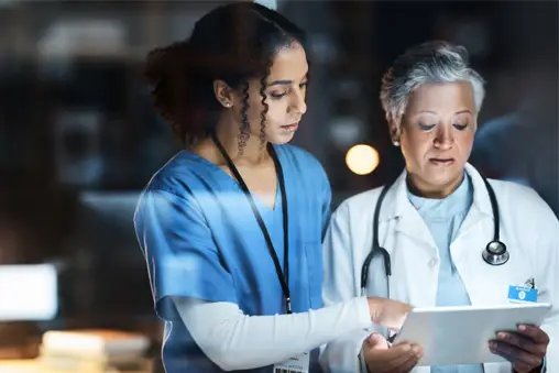 Nurse and doctor reviewing patient information on a digital tablet in a hospital setting.