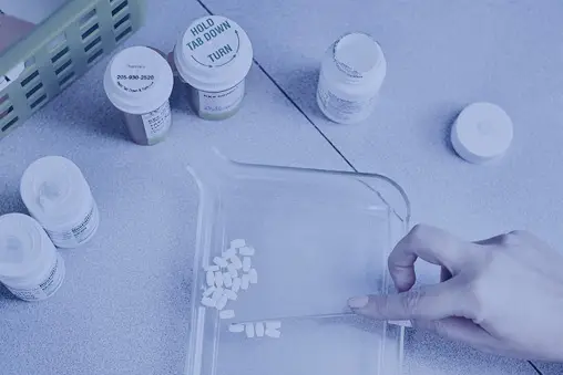 Pharmacist counting prescription pills on a tray with medication bottles in the background.