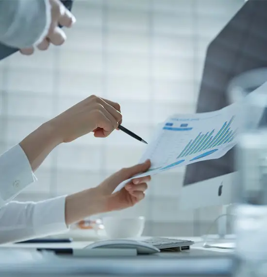 Close-up of hands reviewing financial data and growth charts on a printed report at a modern office desk with computer.