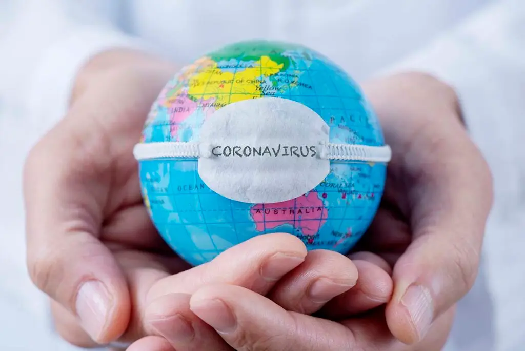 Hands holding a small globe wearing a face mask labeled coronavirus, symbolizing the global impact of the pandemic
