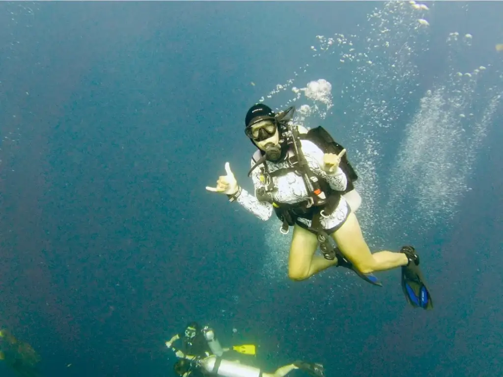 Laura scuba diving underwater in blue water, giving a relaxed hand signal