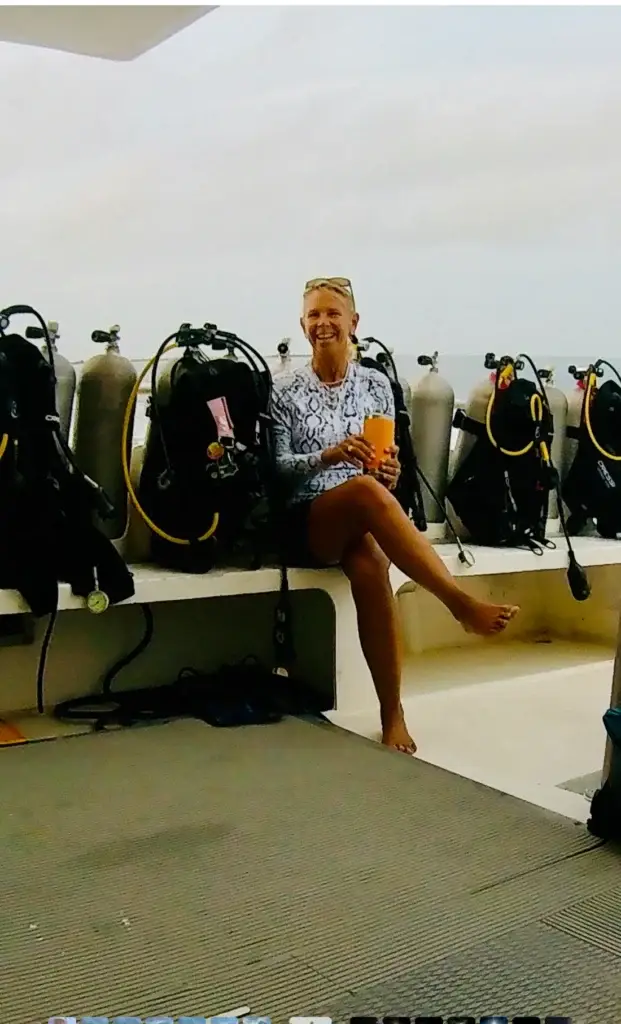 Laura smiling on a dive boat beside a row of scuba tanks